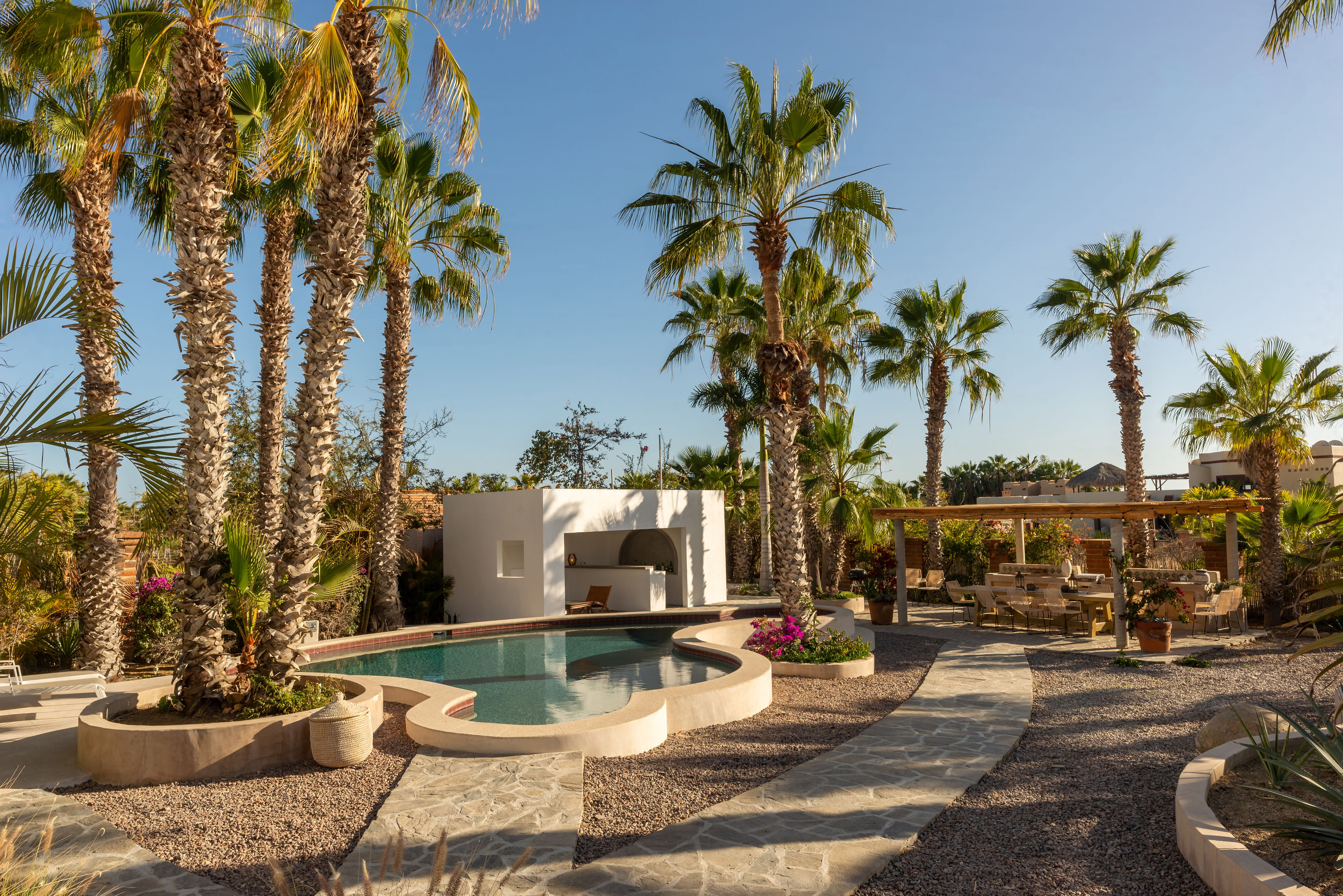 The saltwater pool and hot tub among the palms, with the white cabana on one side and the shaded dining pergola on the other